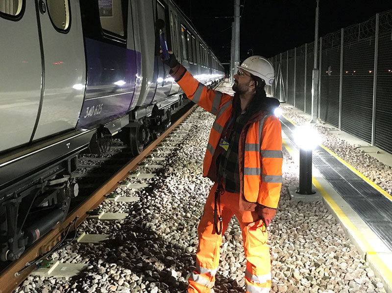 Technician taking sound readings beside train.