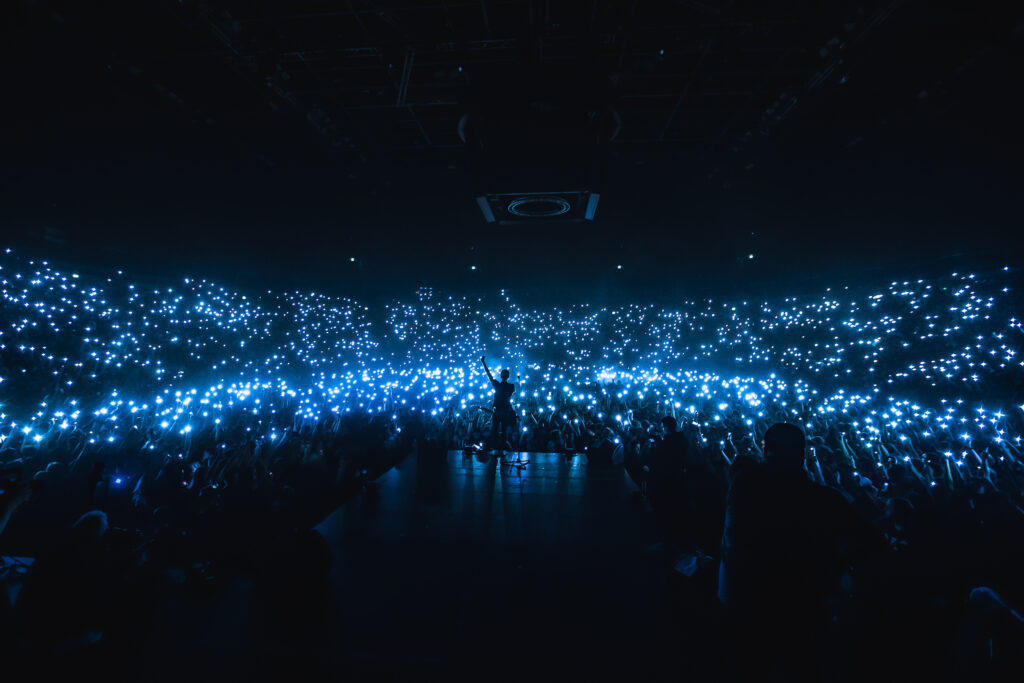 singer on stage in large event , dark venue where the audience is holding up blue lights